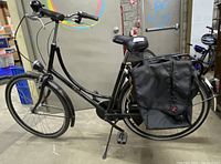 Full side profile of black step-through bicycle with rear panniers, metal fenders, kickstand and accessories