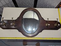 Full view of the Ethan Allen hall mirror coat rack showing oval mirror and four brass and ceramic hooks on antiqued pine wood panel.