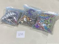 Three plastic bags each filled with multiple colorful fashion bracelets made of various beads including purple, yellow, multicolored, and metal accents.