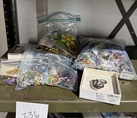 Photo showing multiple plastic bags and boxes containing various pins and a dragonfly keychain on a metal shelf.