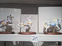 Three Lenox carousel horse figurines on wooden bases with boxes behind them.