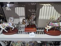 Lot of three Lenox collectable carousel horse figurines on a shelf, each on wooden bases with brass poles and decorative details.