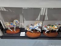 Three Lenox collectible carousel horse figurines on wooden bases displayed together, showing varying designs and colors.