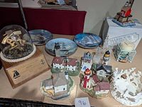 Lot of Harbour Lights lighthouse statues, Franklin Porcelain clipper ship plates, nautical candle holders, and maritime glass dome collectible on wooden base.