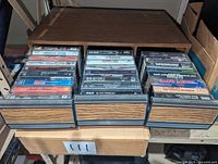 Faux wood cassette storage box with three drawers, each filled with assorted cassette tapes featuring visible titles and artists.
