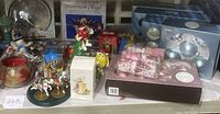 Photo shows multiple Christmas ornaments including M&M characters, small Christmas-themed figurines, boxed Martha Stewart ornaments, and other holiday decorations on a shelf.