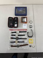 Top view showing whole lot on table including Luminox watch in case, Croton repair kit box, two metal watch straps, six assorted watches lying flat, two watch faces, plastic bezel and parts.