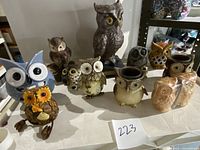 Top view of the assortment of ceramic owl figurines and owl candle holders on display including larger and smaller owls, with some detail of colors and decoration
