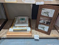 Stack of multiple picture frames on shelf including 11x14 black bordered frame, wooden frames and collage frame.