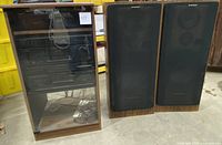 Full view of the Pioneer stereo cabinet with two floor-standing speakers to the right. Cabinet door is closed, housing stereo components inside. Speakers show some damage to the cloth covers.