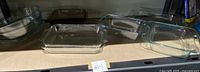 Six clear rectangular Pyrex casserole dishes and pie dishes without lids on a shelf