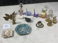 Photo showing entire assortment of vintage decorative items including brass butterfly, ceramic geisha figure, ceramic cats, person figure, brass bells, metal ashtray, German ceramic creamer, and ceramic sheep figurines.