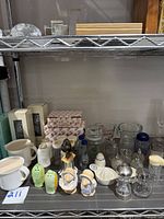 Wide view of vintage salt and pepper shakers, Tupperware creamer, glass oil lamps, and other kitchen items on wire shelf