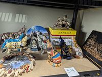 Overview of multiple wolf-themed resin statues in varied colors and designs, a circular plate with wolf imagery surrounded by feathers, and other wolf decor items on display.