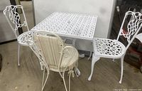 Photo showing the full set of one white wrought iron table and three chairs, highlighting their design and overall condition.