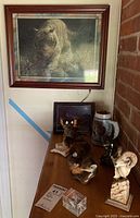 Wide view of framed tiger print above wood table holding animal figurines, ceramic mug stein, and acrylic display cube.