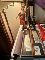 Framed art panels, traditional dancer figurine, metal vases on table next to lamp, partially rolled scroll visible