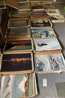 Multiple boxes filled with stacks of medium-sized glossy photographic prints arranged on the floor, showing a variety of landscape and nature scenes.