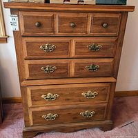 Front view of the wooden dresser showing all seven drawers with brass hardware, warm brown finish, and wood grain.
