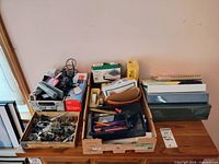 Photo of bulk office supplies including power cords, staplers, hole punches, binders, folders, and paper organizing tools on a wooden table.