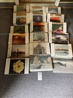 Photo showing 25 unframed photographic prints laid out on the floor, depicting a variety of landscape and nature scenes including cityscapes, ocean views, and flowers, some photos are inside protective sleeves.