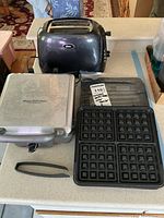 Photo showing the Cuisinart Belgian waffle maker with its removable pancake plate beside an Oster 2-slice toaster on a countertop.
