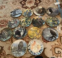 Overview of 14 Driscoll collector plates featuring various birds and winter/nature scenes, arranged on patterned carpet.