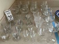 Overview of multiple clear glassware pieces arranged showing goblets, tumblers, and sherry glasses with a price tag