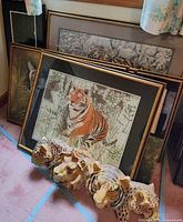 Multiple framed tiger artworks with layered framing in black and gold, placed on carpeted floor.