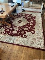 Full view of the rectangular hand made wool rug with Persian floral design in red and cream, partially under wooden furniture.
