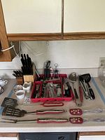 View of variety of kitchen cutlery, flatware, and tools arranged on kitchen countertop.