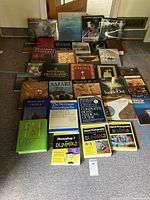 Photo showing full assortment of 28 plus books on carpeted floor arranged in rows, including photographic, health, geography, history topics.