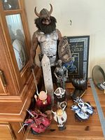 Large Viking figurine with silver chest armor, holding a sword and a shield, standing next to a tall tower model, smaller Viking and knight figurines, Viking ship model, and the Historical Atlas of Knights & Castles book in the background