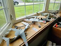 Photo showing several WWII themed military model aircraft and helicopters arranged on a windowsill, including varied paint schemes and markings of Red Star, Cross, and Rising Sun.