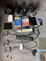 Full view of mixed electronics and accessories laid out on carpet including toners, power strips, external hard drive, cables, tablet, and boxed software package