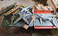 Wide shot of diverse model airplanes and ships displayed on tables, showing various military and commercial designs.