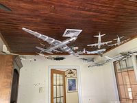 View of the collection of 13 model airplanes hanging from a ceiling in a room, showing various sizes and types of silver and metallic aircraft models.