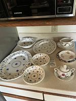 Overall view of entire set including platters, bowls, plates, gravy boat, sugar bowl, and covered dish placed on countertop under microwave.