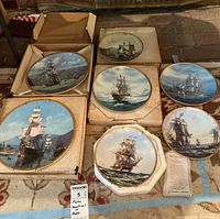 Overview of all eight maritime ship collector plates showing various ships and packaging boxes in a display on carpeted floor.