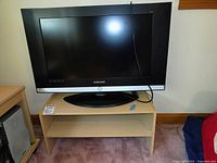 Front view of Samsung 32-inch TV on light wood stand showing screen and base, no accessories visible.