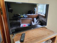 Samsung 32-inch TV with remote on wooden table, reflective screen showing room interior.