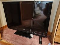 Front view of Sony 40 inch LCD TV with power cord hanging, remote placed on carpet, showing screen and bezel details.