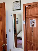 View of the Sunbeam wall clock and full-length mirror mounted on the wall between wooden doors, showing clock with green and gold frame and Roman numerals.