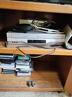 Front and angled view of Toshiba SD-V393SU1 DVD/VCR combo showing front panel, cables, remote, and DVDs below unit on shelf