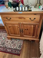 Front view of the wooden sideboard showing double doors, drawer, and stone top with items on it.