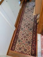 Runner rug with repeating diamond and floral motifs along a hallway floor, next to wood paneling and white walls.