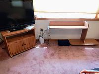 Front view of the wooden TV stand with cabinet doors and small desk with shelf next to it on pink carpet.
