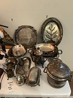 Full set of vintage metal trays and serving pieces spread on surface showing varied shapes and sizes with tarnishing and patina.