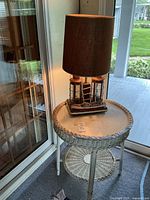 Full view of vintage round wicker table painted white with glass top, showing integrated lamp with nautical ship design and brown lampshade.