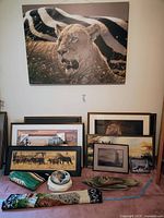 Large canvas of lioness in front of zebras, multiple smaller framed wildlife prints and art pieces on the floor including animal sculptures and textiles